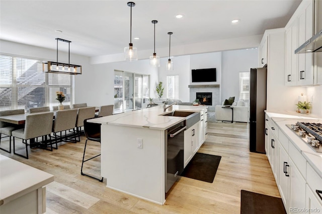 kitchen with white cabinetry, dishwasher, hanging light fixtures, fridge, and a center island with sink