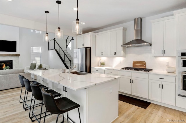 kitchen with white cabinetry, an island with sink, wall chimney exhaust hood, and appliances with stainless steel finishes