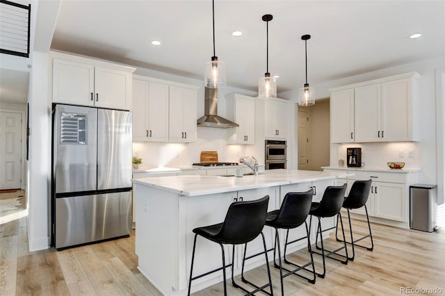 kitchen featuring appliances with stainless steel finishes, a center island with sink, white cabinets, and decorative light fixtures