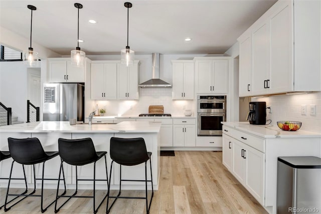 kitchen featuring white cabinetry, wall chimney exhaust hood, stainless steel appliances, and a center island with sink