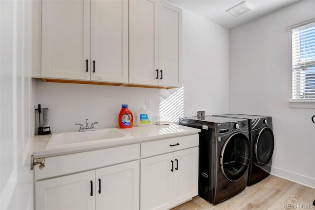 laundry room featuring cabinets, washing machine and dryer, sink, and light hardwood / wood-style flooring