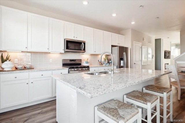 kitchen featuring wood finished floors, a sink, white cabinetry, a center island with sink, and appliances with stainless steel finishes