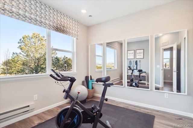 workout area with baseboards, visible vents, wood finished floors, and baseboard heating
