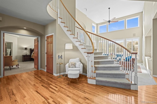 stairway with arched walkways, a high ceiling, a ceiling fan, wood finished floors, and baseboards