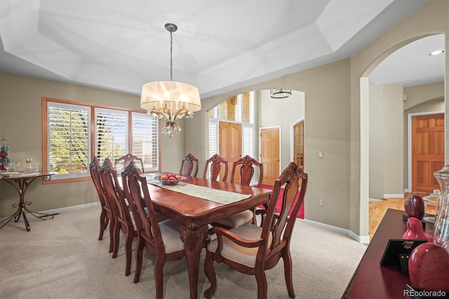 dining area with light carpet, baseboards, arched walkways, and a tray ceiling