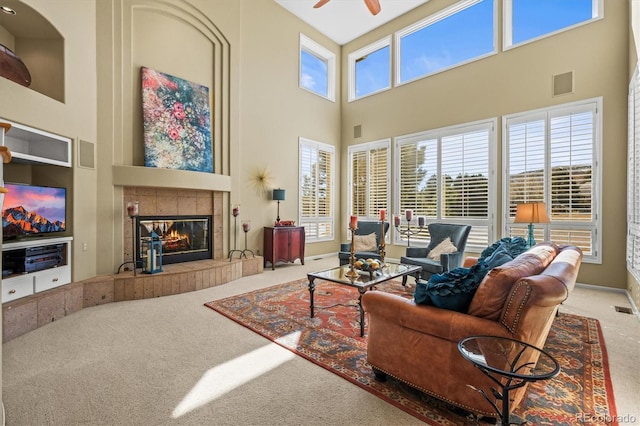 carpeted living area with a ceiling fan, a tile fireplace, a healthy amount of sunlight, and visible vents