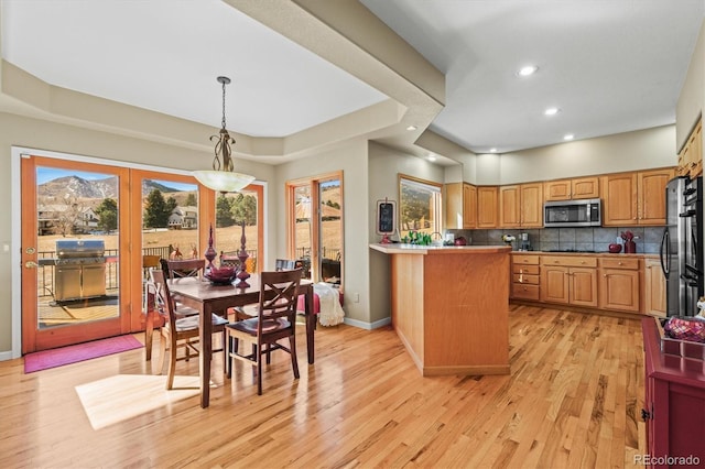 kitchen featuring hanging light fixtures, decorative backsplash, appliances with stainless steel finishes, light wood-type flooring, and a peninsula