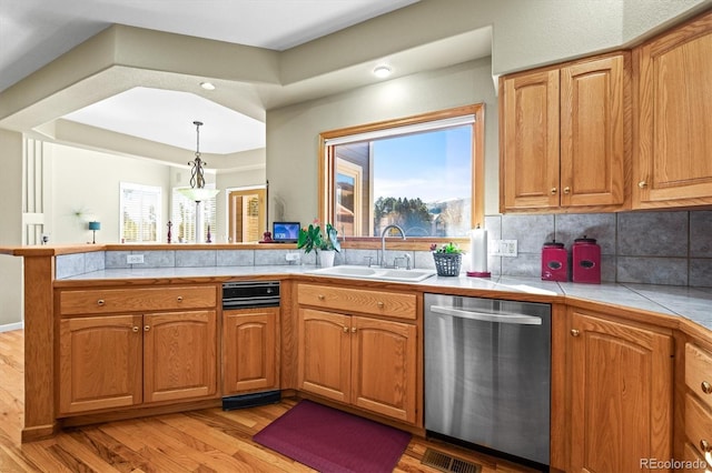 kitchen with tasteful backsplash, a peninsula, light wood-type flooring, stainless steel dishwasher, and a sink