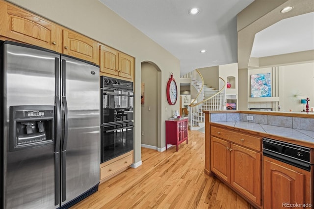 kitchen featuring tile countertops, recessed lighting, dobule oven black, light wood-style floors, and stainless steel fridge