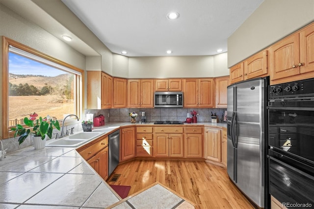 kitchen featuring tile countertops, light wood finished floors, decorative backsplash, a sink, and black appliances