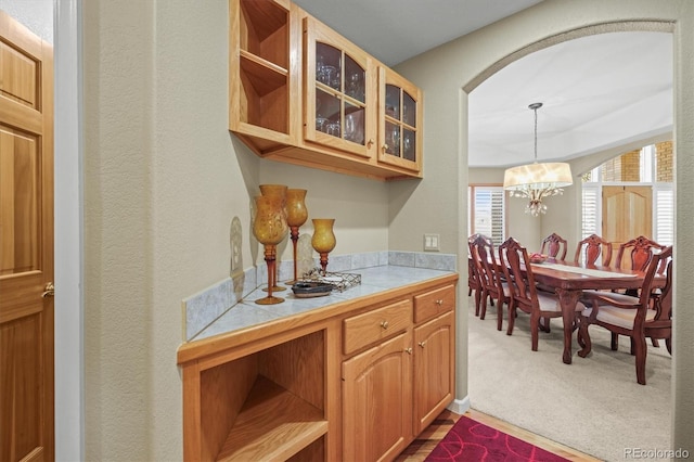 kitchen with carpet floors, hanging light fixtures, open shelves, glass insert cabinets, and an inviting chandelier