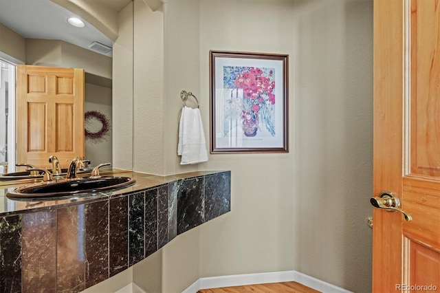 bathroom with baseboards, visible vents, a sink, and wood finished floors