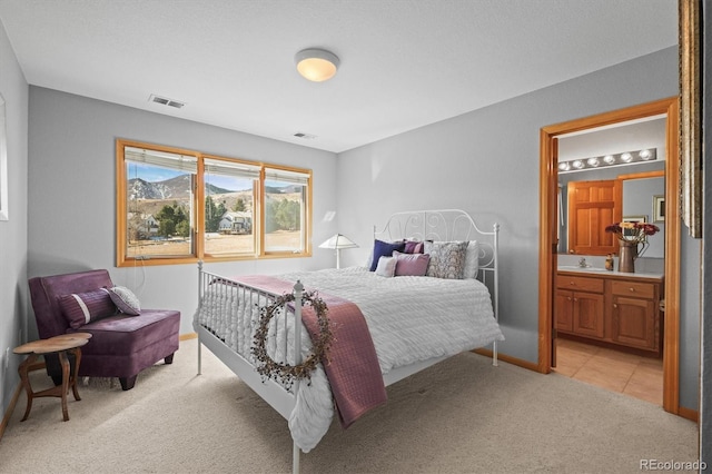 bedroom with baseboards, connected bathroom, visible vents, and light colored carpet