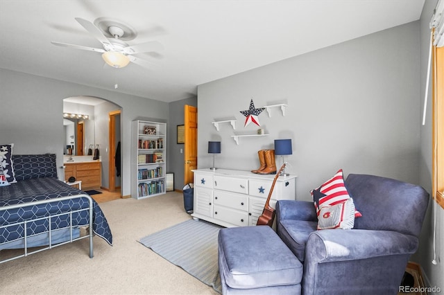 bedroom with arched walkways, light carpet, ceiling fan, and ensuite bath