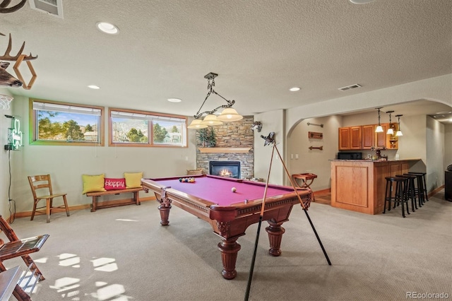 playroom featuring arched walkways, a stone fireplace, a textured ceiling, and light carpet