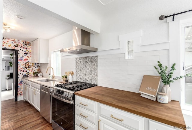 1946 Xenia St, Denver, CO 80220 - kitchen featuring stainless steel appliances, wall chimney exhaust hood, wood counters, white cabinets, and a textured ceiling