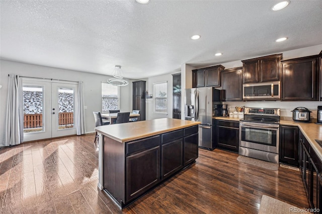 kitchen featuring french doors, stainless steel appliances, dark wood-type flooring, a kitchen island, and hanging light fixtures