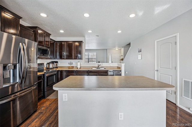 kitchen with a textured ceiling, a kitchen island, dark hardwood / wood-style floors, and appliances with stainless steel finishes