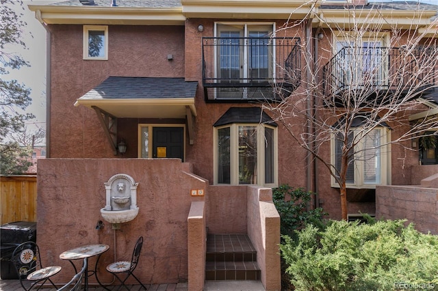 multi unit property with a shingled roof, a balcony, and stucco siding