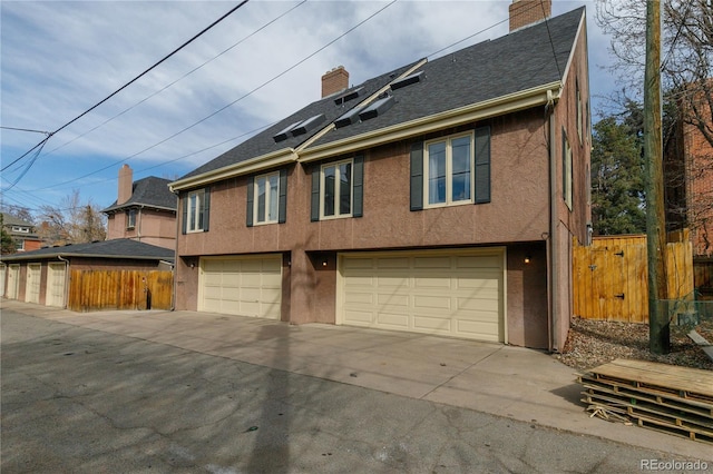 view of front of home featuring stucco siding, a chimney, a garage, and fence