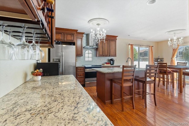 kitchen with light stone countertops, wall chimney exhaust hood, a kitchen island, stainless steel appliances, and a notable chandelier