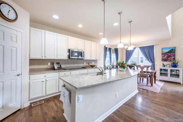 kitchen with light stone countertops, backsplash, pendant lighting, white cabinetry, and an island with sink