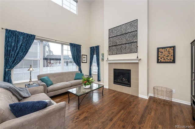 living room with a fireplace, a towering ceiling, a healthy amount of sunlight, and hardwood / wood-style flooring