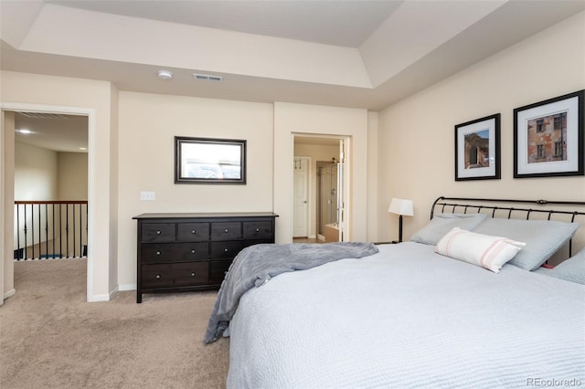 bedroom featuring a tray ceiling, ensuite bath, and light colored carpet