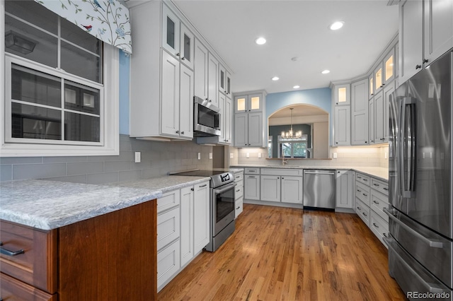 kitchen with pendant lighting, white cabinets, decorative backsplash, light wood-type flooring, and appliances with stainless steel finishes