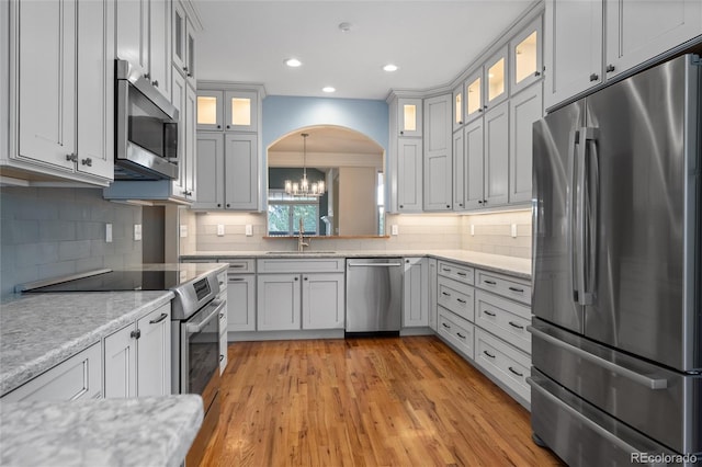 kitchen featuring sink, tasteful backsplash, light hardwood / wood-style flooring, pendant lighting, and appliances with stainless steel finishes