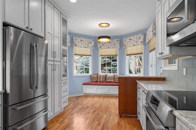 kitchen with decorative backsplash, light stone countertops, stainless steel appliances, pendant lighting, and light hardwood / wood-style flooring