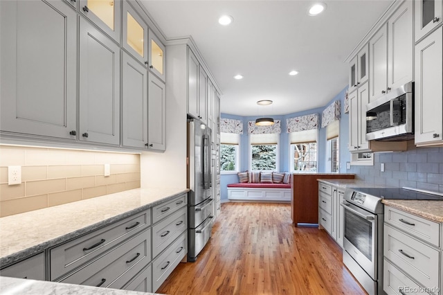 kitchen with tasteful backsplash, light stone countertops, light hardwood / wood-style floors, and appliances with stainless steel finishes