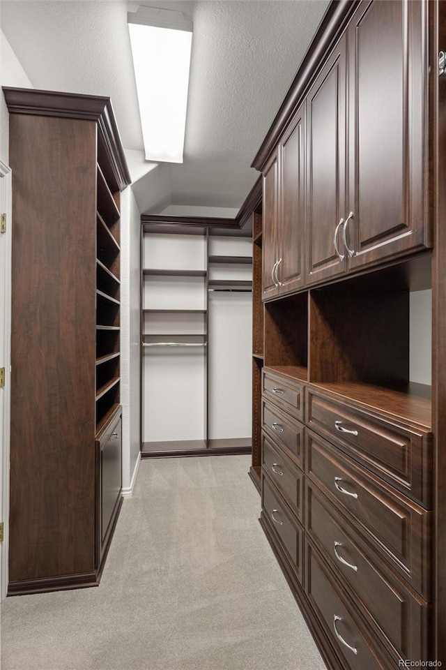 walk in closet with light colored carpet and vaulted ceiling