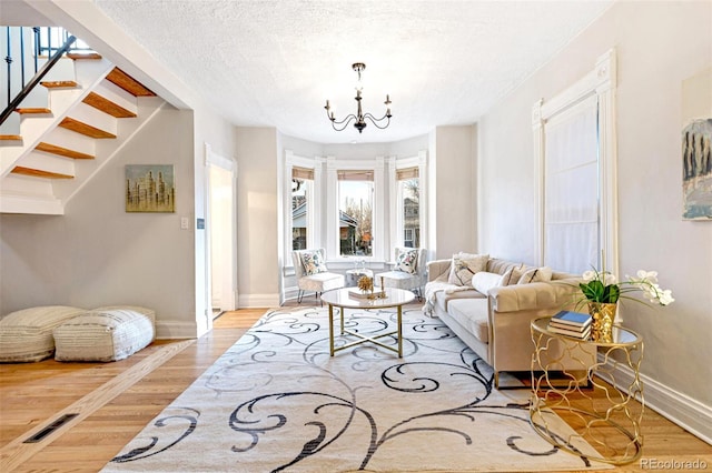 living room featuring a textured ceiling, wood finished floors, a chandelier, baseboards, and stairs