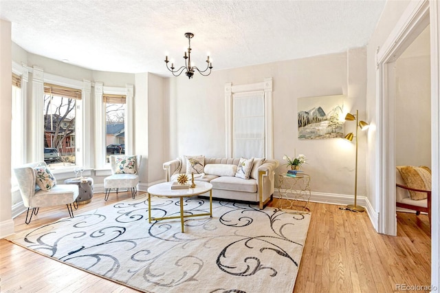 living room featuring light wood-style floors, baseboards, a chandelier, and a textured ceiling