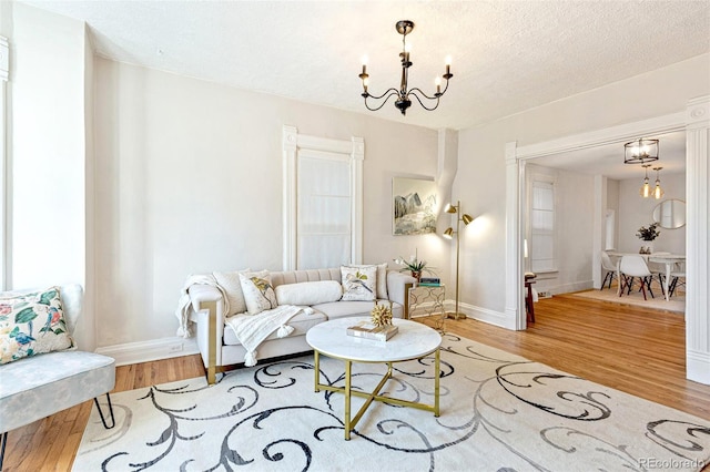 living room with an inviting chandelier, baseboards, light wood finished floors, and a textured ceiling