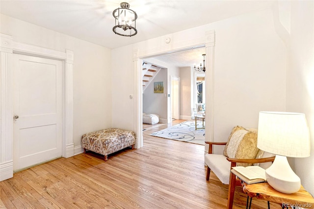 sitting room featuring a chandelier, stairway, light wood-style flooring, and baseboards