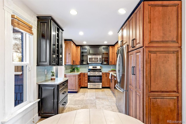 kitchen with appliances with stainless steel finishes, brown cabinetry, backsplash, and glass insert cabinets