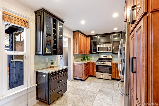 kitchen with stainless steel appliances, recessed lighting, backsplash, glass insert cabinets, and light stone countertops