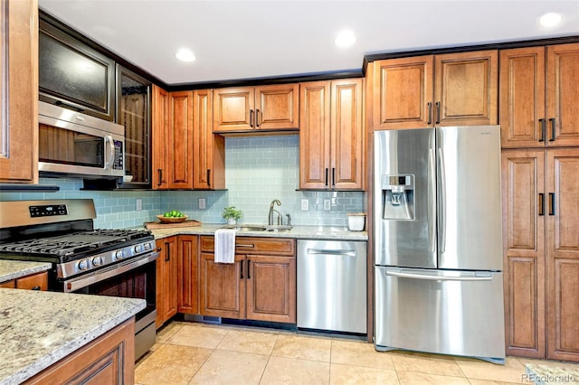 kitchen with light stone countertops, stainless steel appliances, a sink, and brown cabinetry