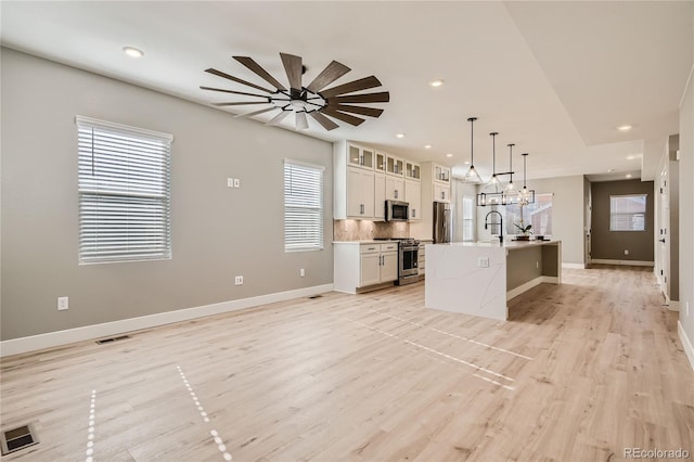 kitchen with white cabinetry, an island with sink, decorative backsplash, hanging light fixtures, and stainless steel appliances