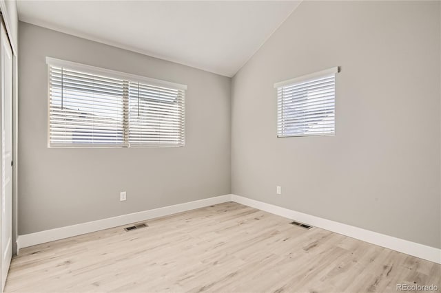 empty room featuring a wealth of natural light, light hardwood / wood-style floors, and vaulted ceiling