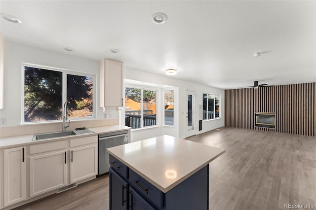 kitchen featuring white cabinetry, dishwasher, sink, a kitchen island, and light wood-type flooring