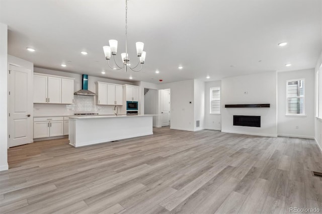 kitchen featuring wall chimney exhaust hood, built in microwave, recessed lighting, open floor plan, and a sink