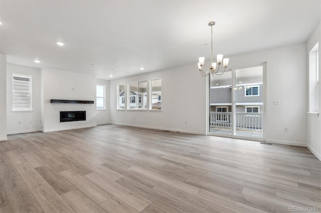 unfurnished living room with a chandelier, light wood-style flooring, recessed lighting, baseboards, and a glass covered fireplace