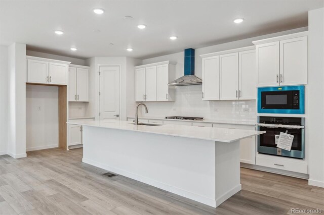 kitchen with oven, wall chimney range hood, a sink, built in microwave, and stainless steel gas stovetop