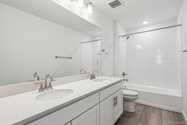 bathroom with wood finished floors, double vanity, toilet, and tub / shower combination