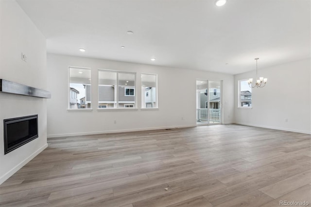 unfurnished living room with a glass covered fireplace, a chandelier, light wood finished floors, recessed lighting, and baseboards