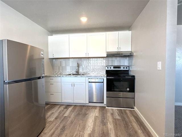 kitchen with sink, white cabinetry, wood-type flooring, appliances with stainless steel finishes, and light stone countertops