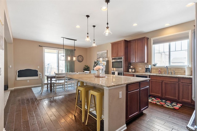 kitchen with a sink, double oven, dark wood-type flooring, a kitchen island, and decorative backsplash
